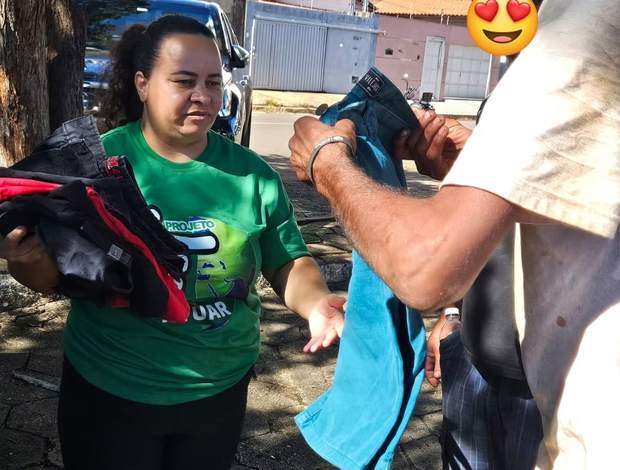 Voluntária do Projeto Atuar entregando roupas a um atendido
